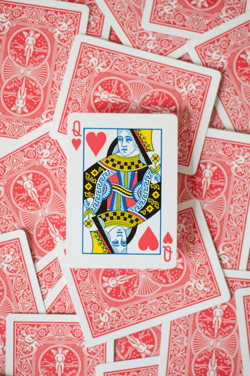 Close-up of Queen of Hearts surrounded by scattered red back playing cards.